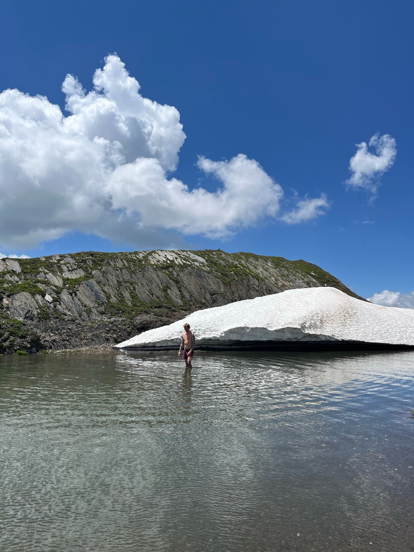 Person watet in einen flachen Bergsee neben einem liegengebliebenen Schneefeld