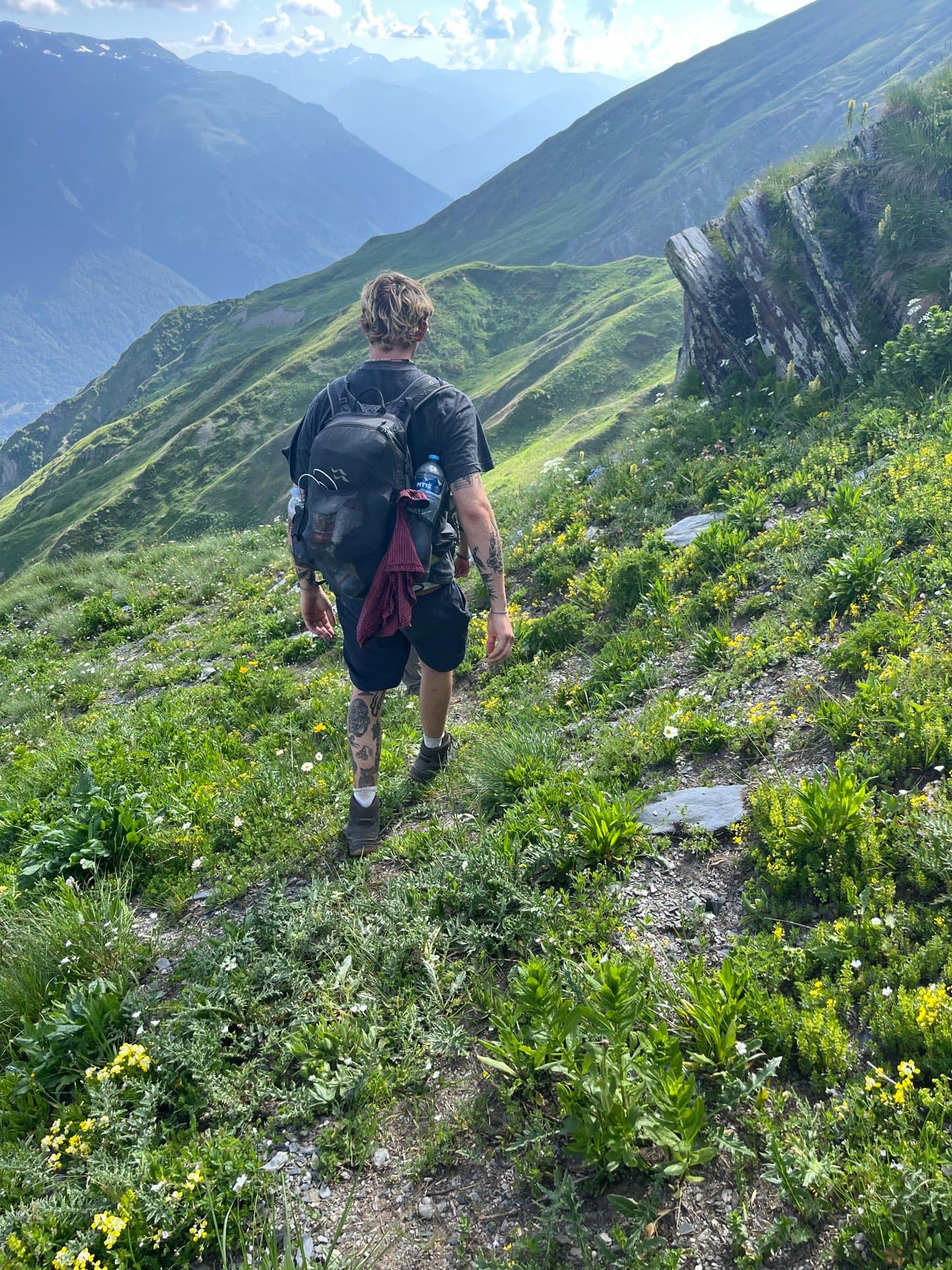 Hiker with a backpack on a narrow path above flowering mountain meadows