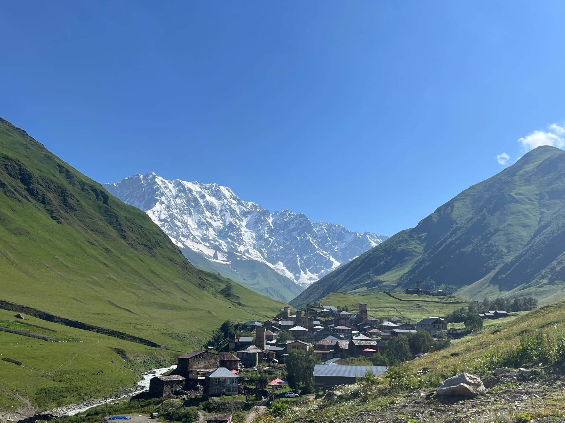 Ushguli zwischen grünen Hängen, dahinter die Gletscherwand des Schchara