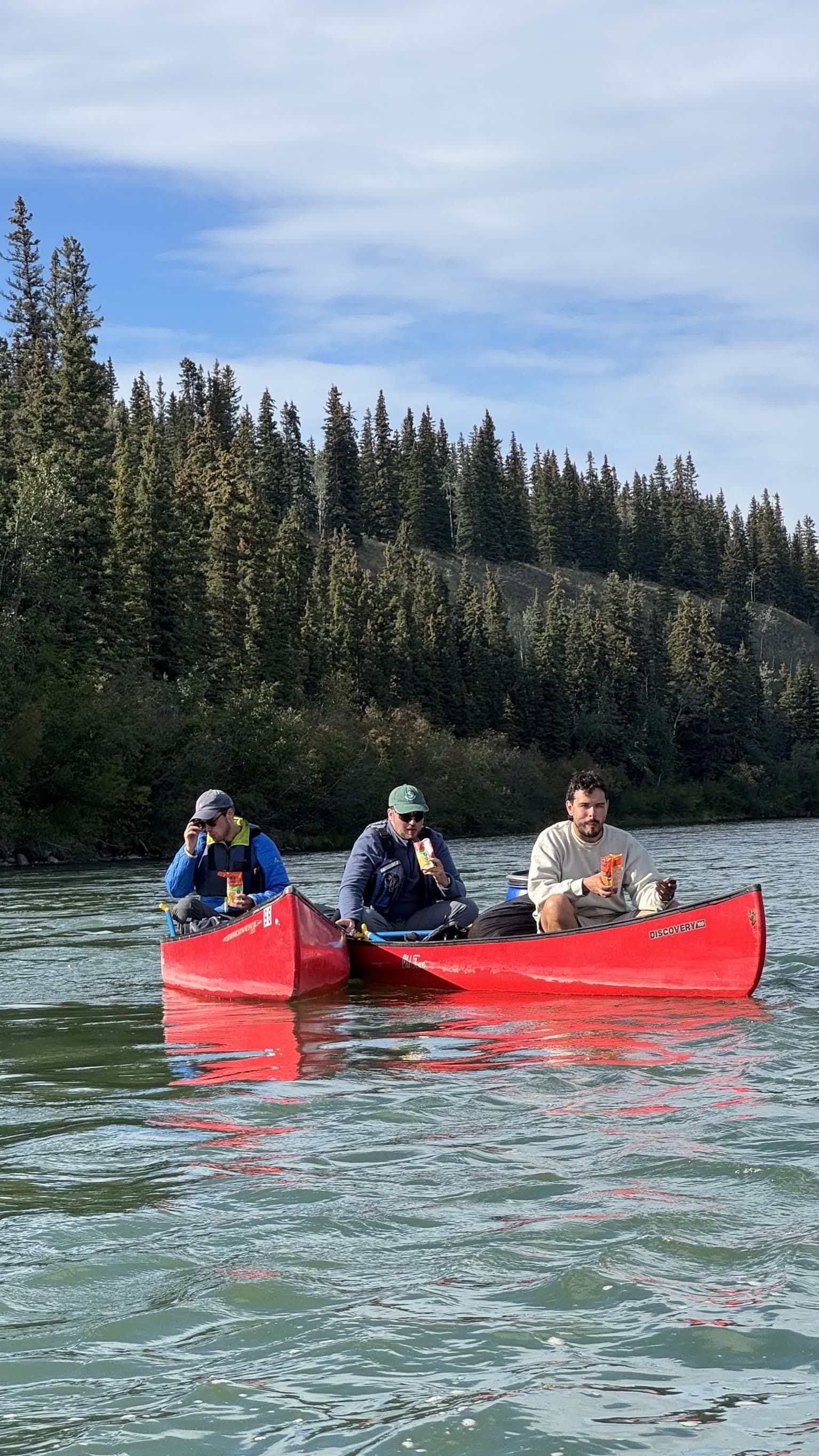 Drei Teilnehmer machen im Kanu eine Snackpause auf dem Yukon River