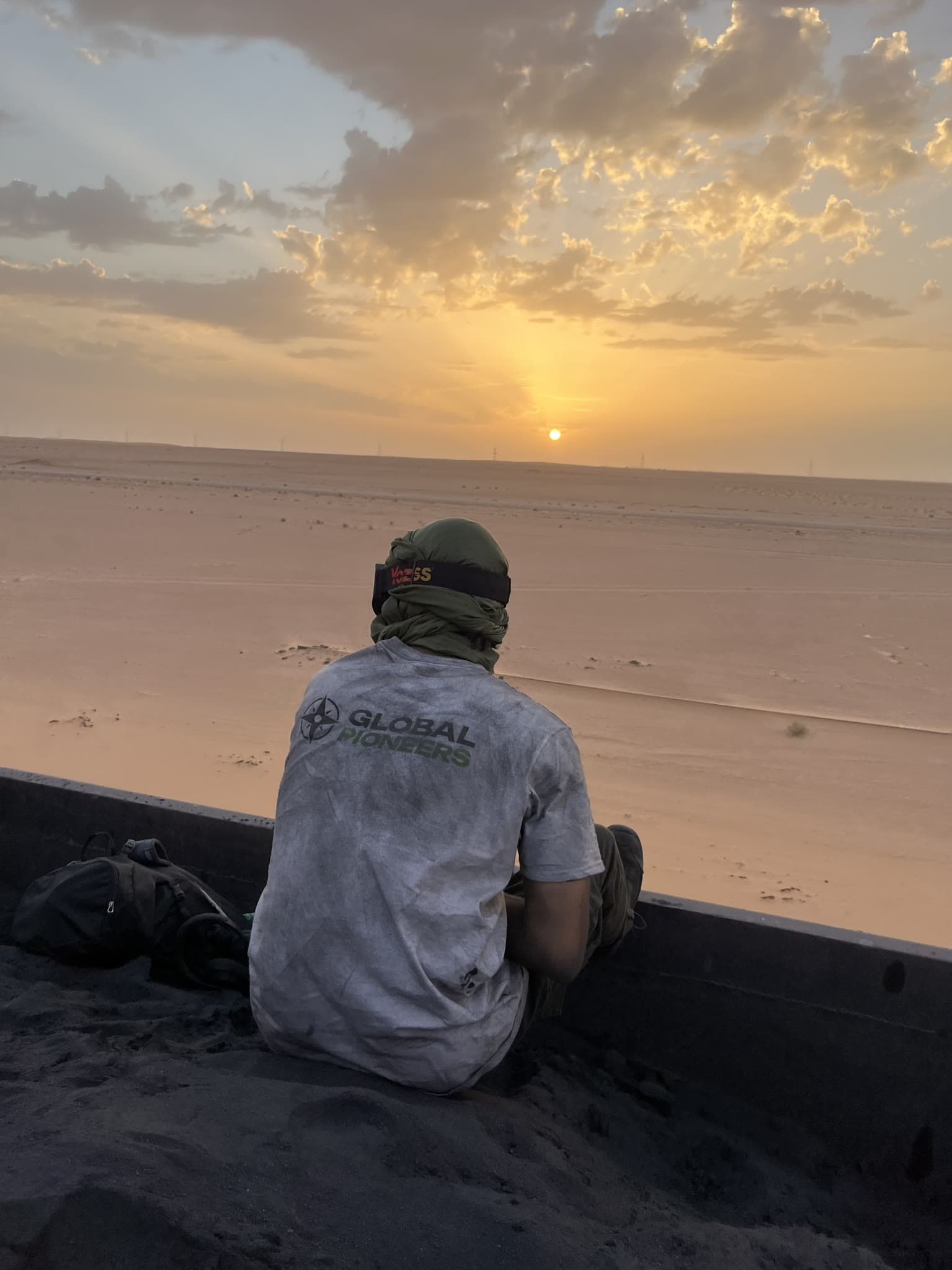 Teilnehmer sitzt auf der Ladefläche und blickt über die Wüste in den Sonnenuntergang