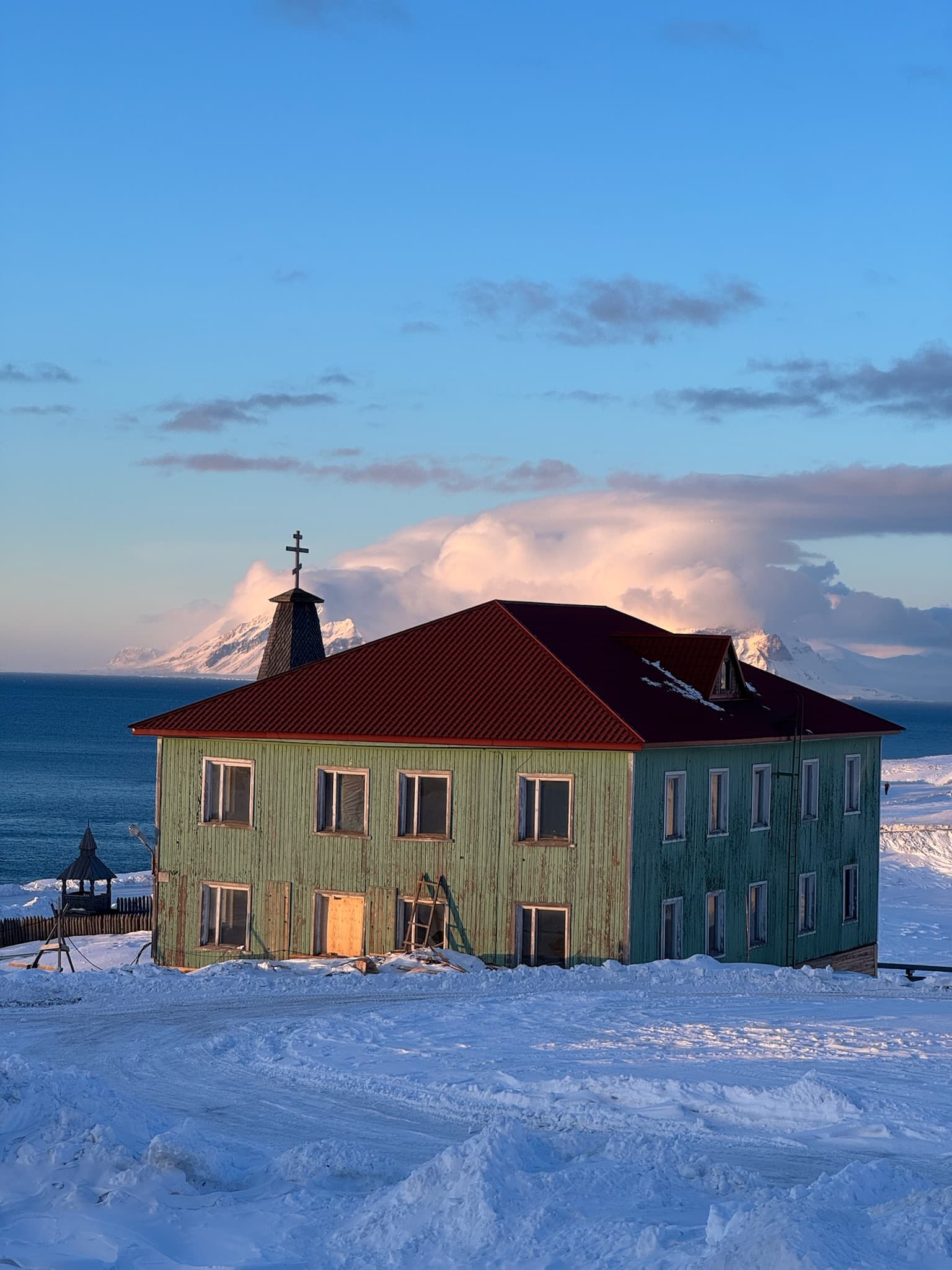 Grün gestrichenes Holzhaus mit orthodoxem Kreuz in der russischen Siedlung Barentsburg bei Sonnenuntergang