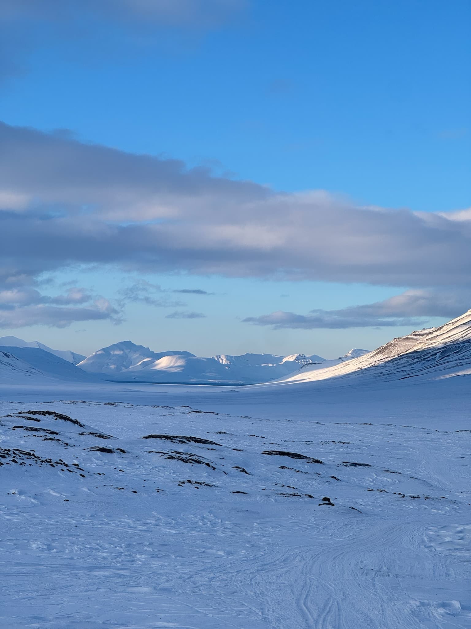 Weites Bergpanorama mit gefrorenem Fjord auf Spitzbergen unter blauem Himmel