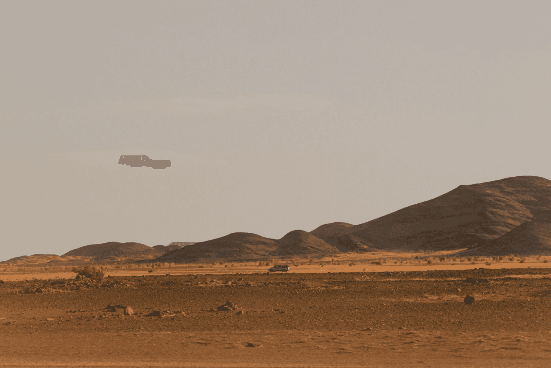 Luftaufnahme eines von schwarzen Felsplateaus gesäumten Sandtals in der Sahara
